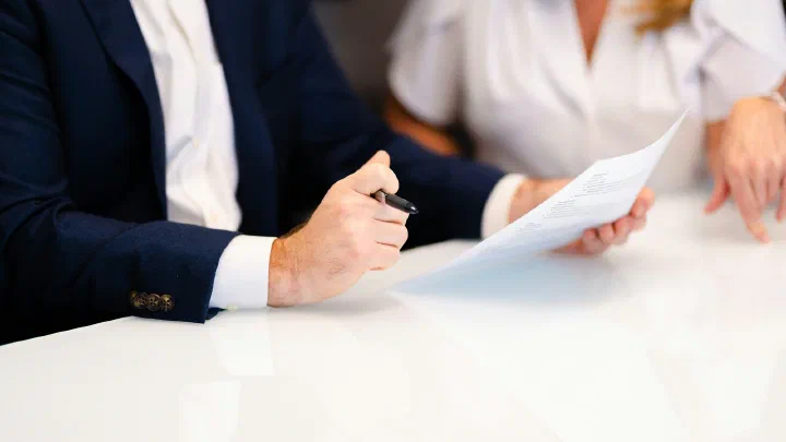 Two people sitting at a white table with printed pages in front of them