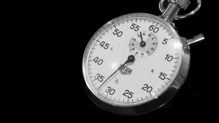 A close-up of an analogue stopwatch face against a black background