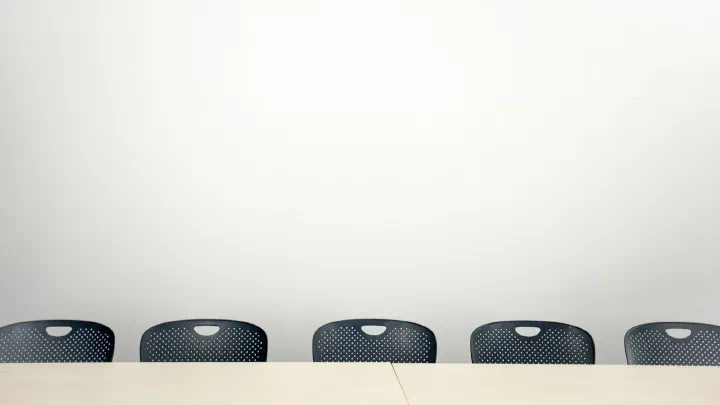 Three black chairs around a small table in an empty white meeting room