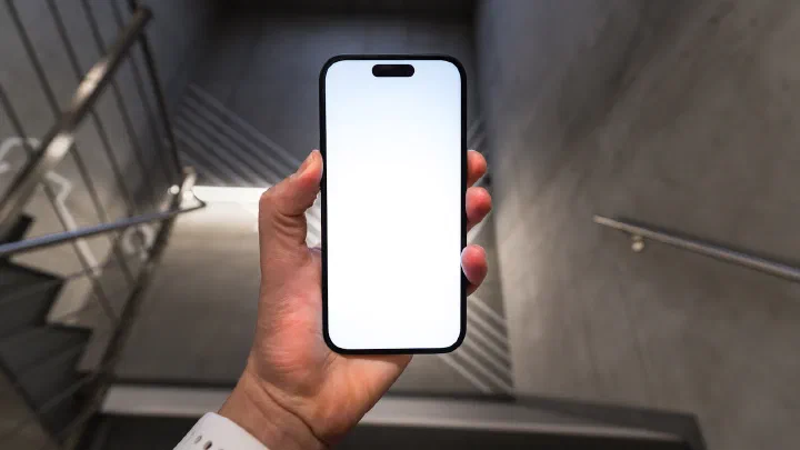 A hand holding a smartphone with a blank screen on a concrete staircase